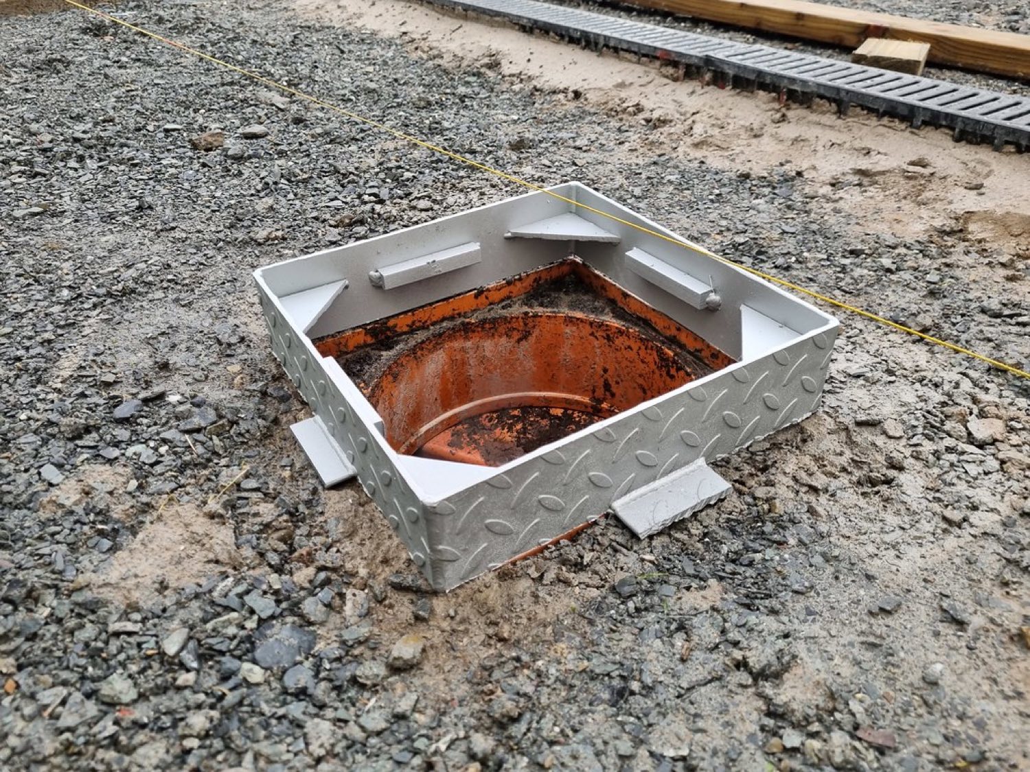 Access cover frame set over a riser on a graded gravel site
