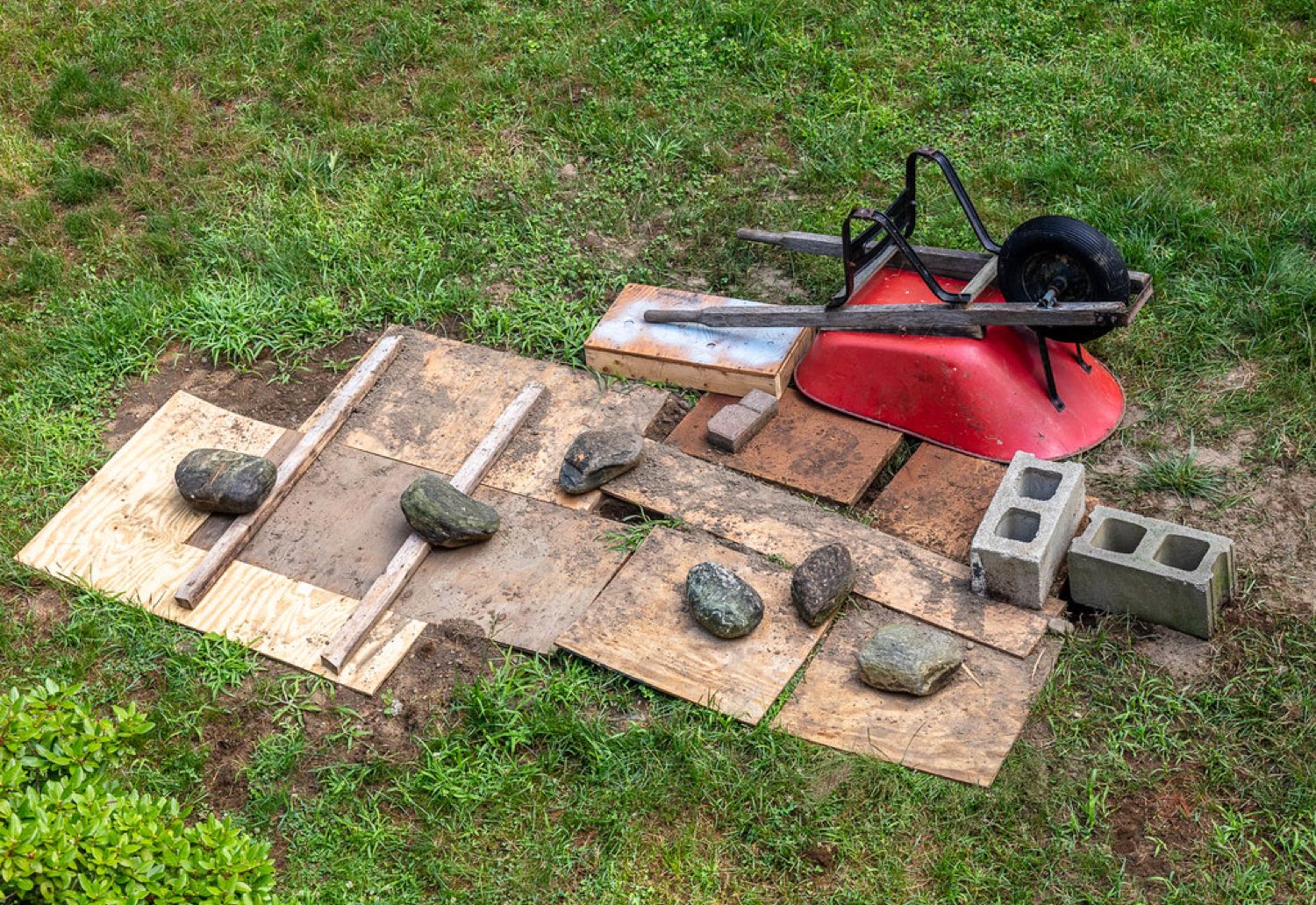 Plywood and stones covering an open excavation in a home lawn